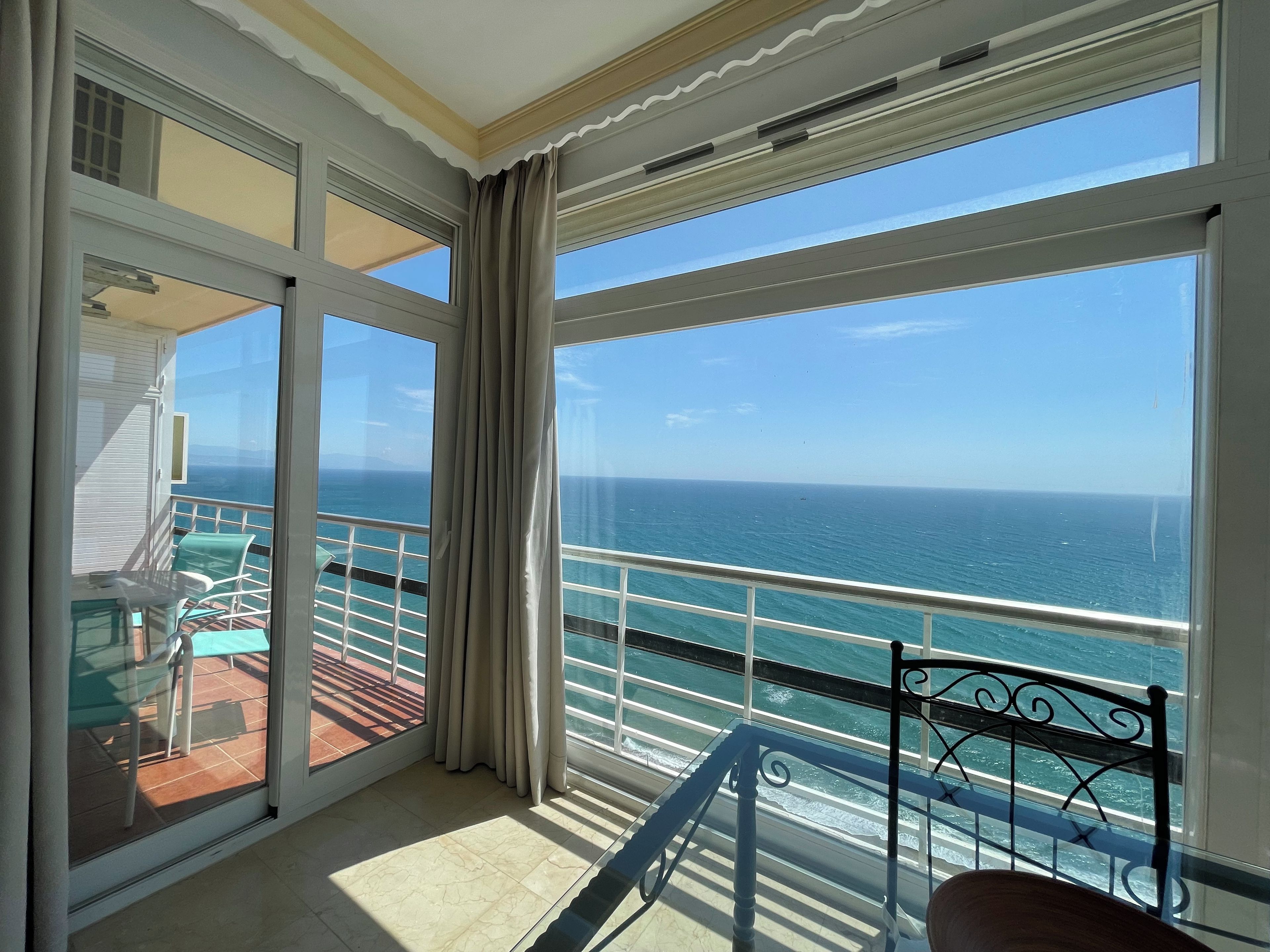 A balcony with a view of the ocean, a chair, and a table.