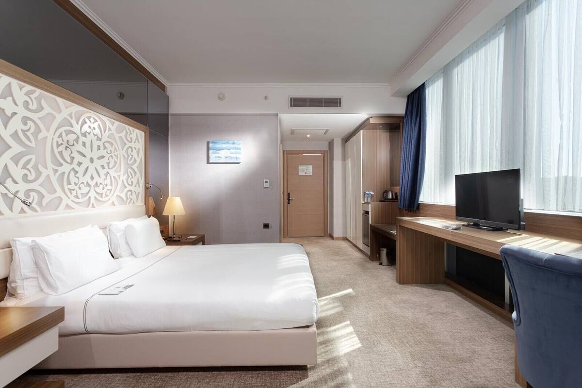 A hotel room with a large bed, a desk with a television, a bathroom, and a decorative wall panel.
