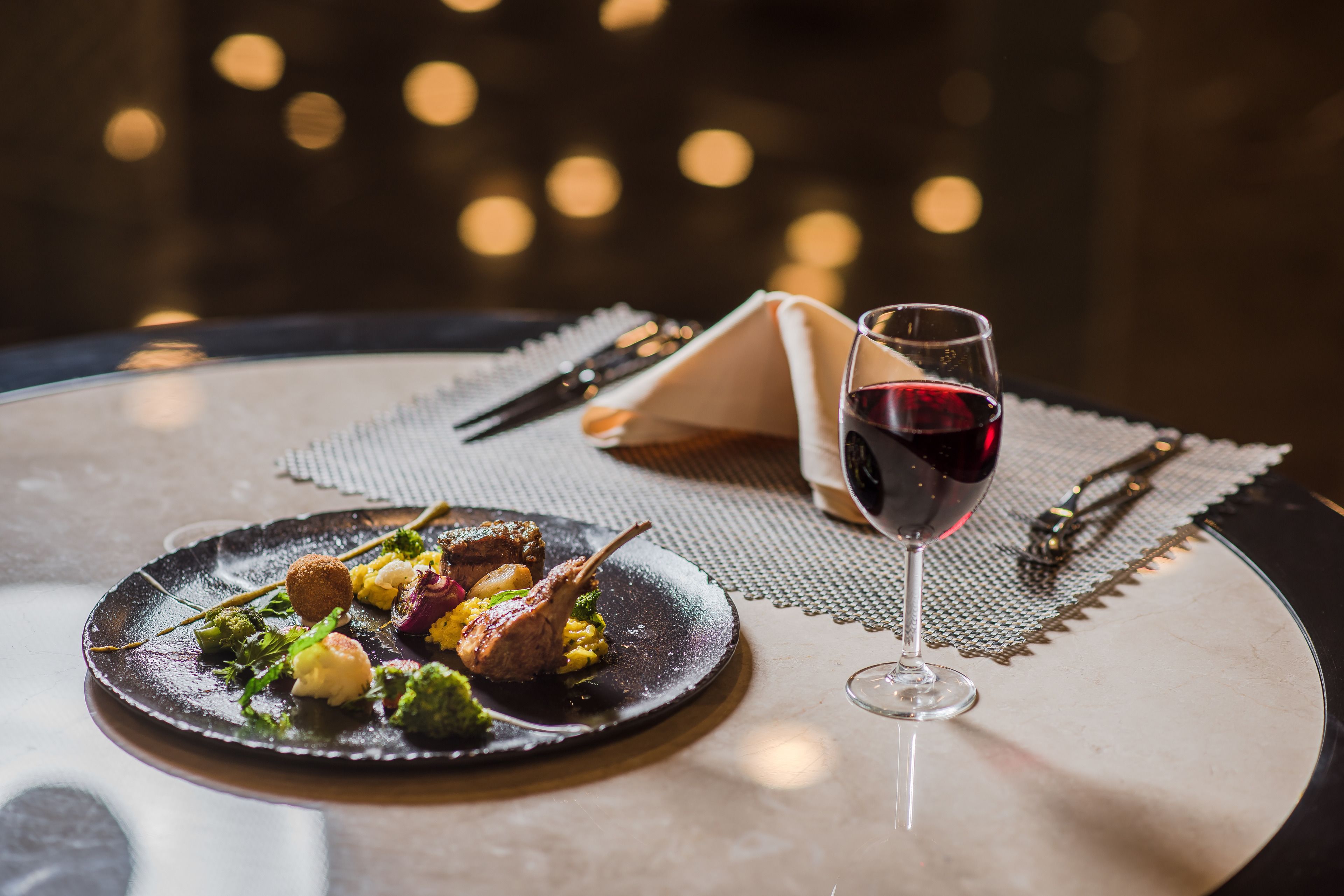 Una mesa con un plato de comida, una copa de vino tinto y cubiertos.