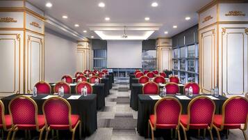 A conference room with rows of tables and chairs, equipped with water bottles, and a large screen at the front.