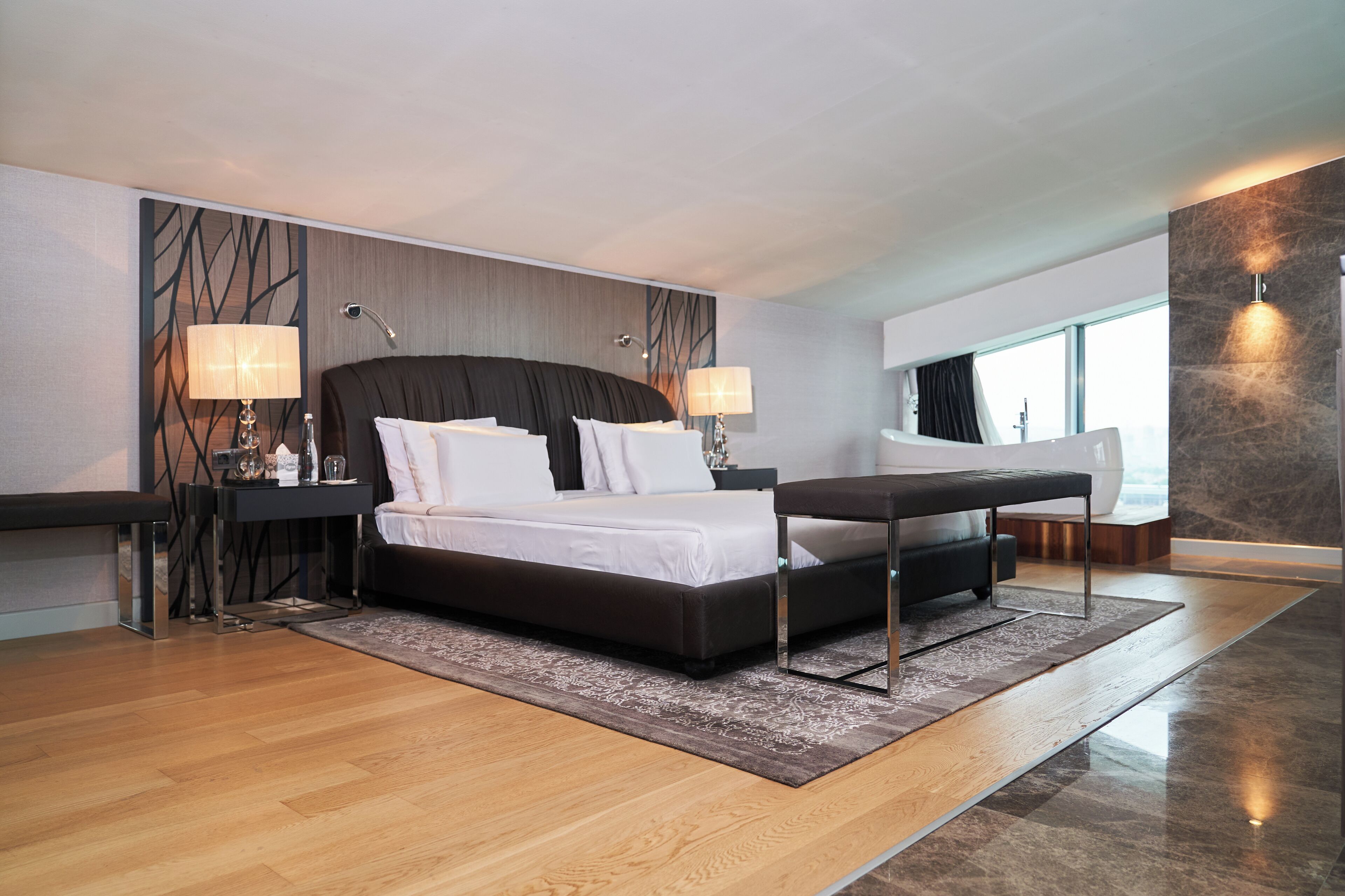 A modern hotel room with a large bed, bedside tables, and a view of the city.