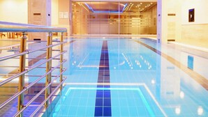 Une piscine intérieure moderne, dotée d’une eau cristalline, entourée d’une paroi en verre et de rampes métalliques.