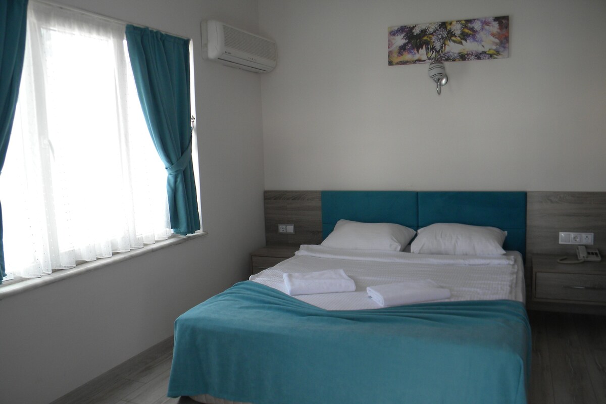 Habitación de hotel con cama, mesita de noche, aire acondicionado de pared y ventana con cortinas.