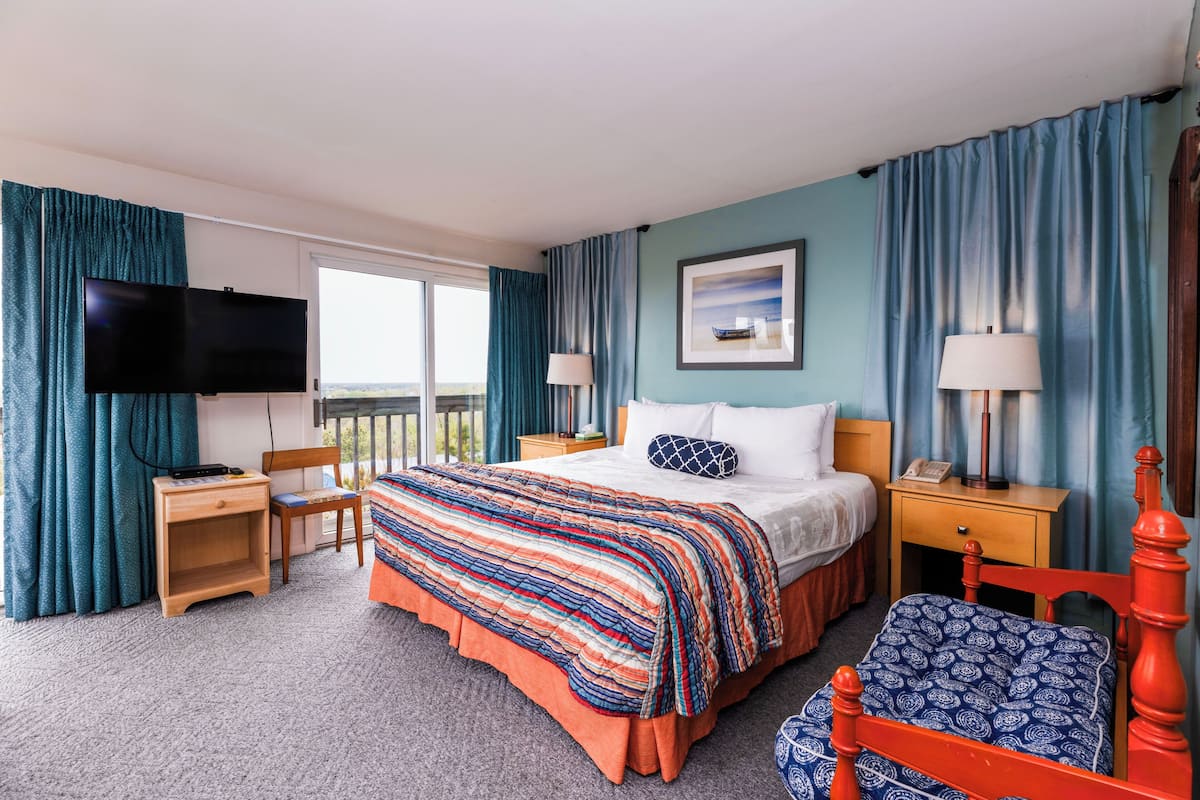 A hotel room with a bed, a TV, a desk, a chair, and a balcony view.