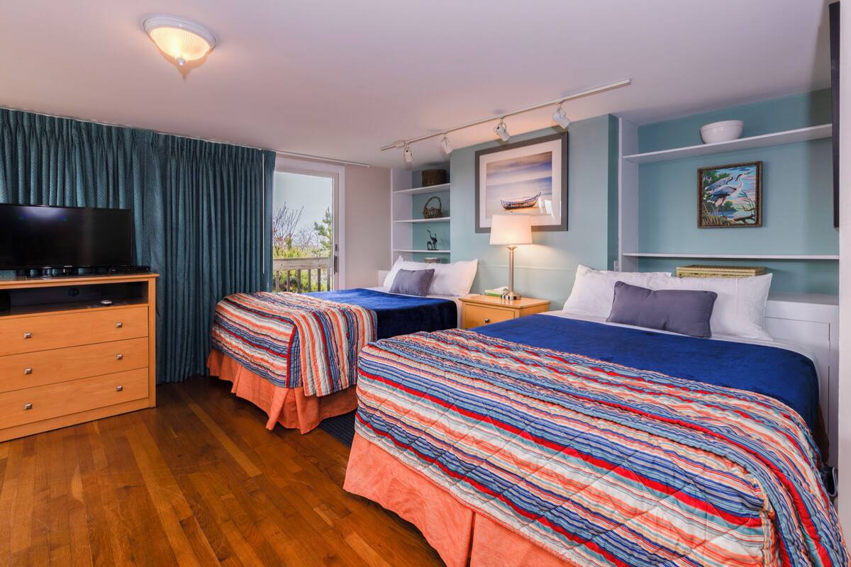 A hotel room with two beds, a TV, wooden dresser, and a balcony view.