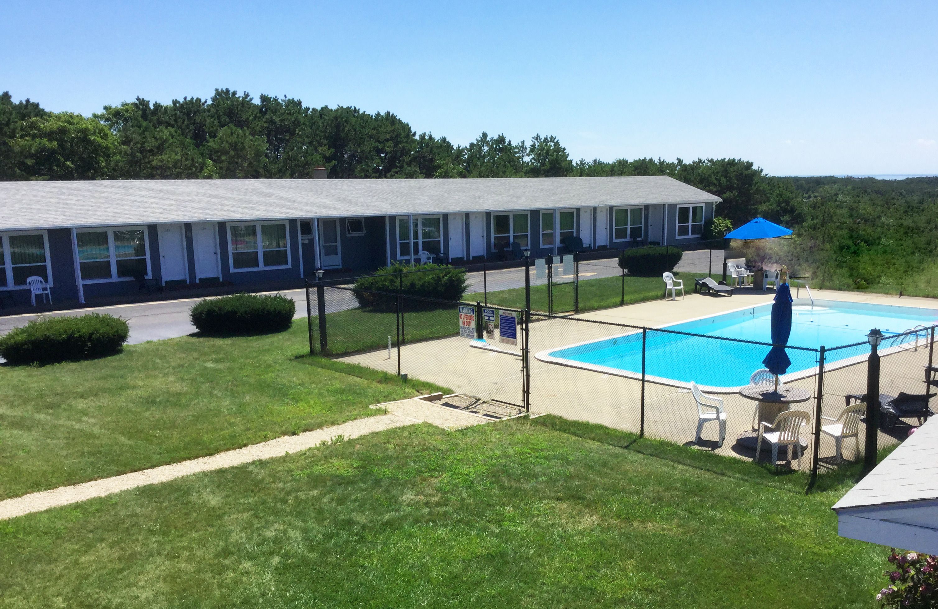 A motel with a swimming pool, outdoor seating, and a view of the surrounding area.