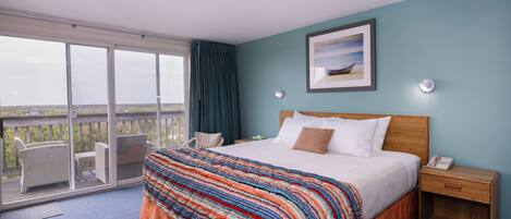 Habitación de hotel con una cama grande, un balcón con mobiliario exterior y vistas al paisaje.