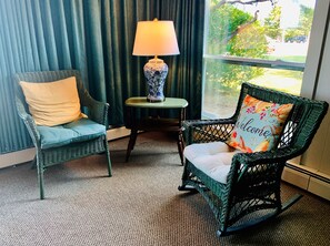 Deux fauteuils en osier avec des coussins, une petite table avec une lampe et une vue sur la verdure à l’extérieur.
