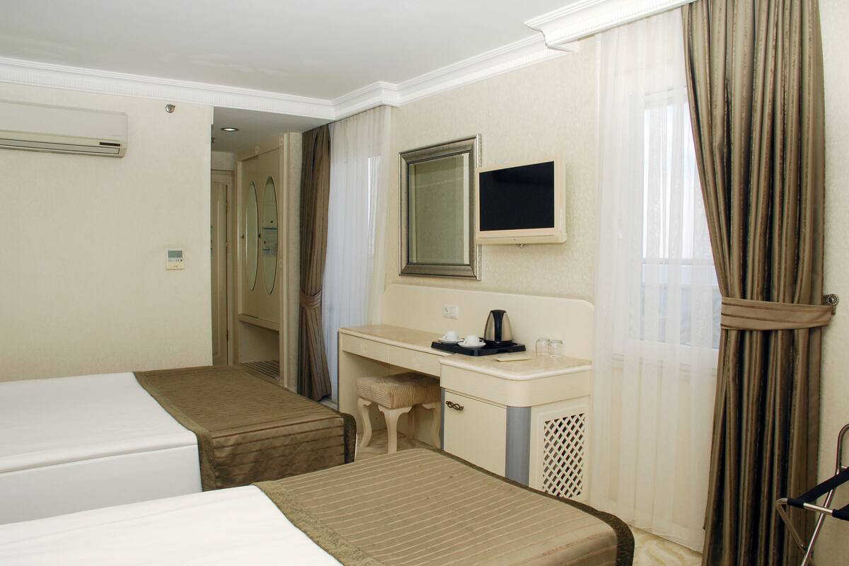 A hotel room with two beds, a small desk with a mirror, a coffee maker, and a window with curtains.