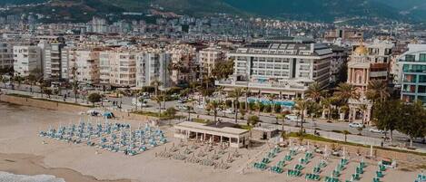 A coastal cityscape with a beach featuring rows of sun loungers and a building with a dome structure.