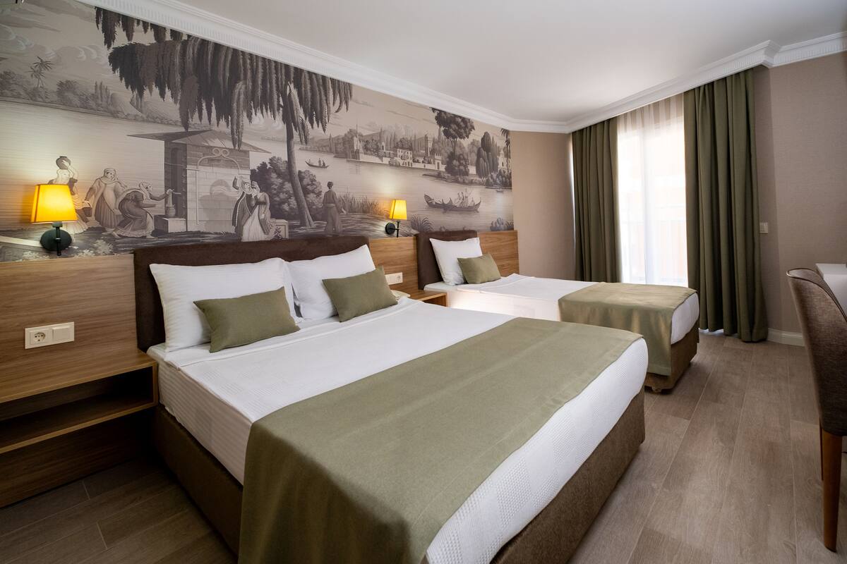 A hotel room with two beds, a mural on the wall, and a view of the outdoors.