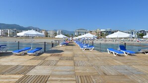 A wooden boardwalk leading to a beach with blue lounge chairs and white umbrellas. - White Gold Hotel & Spa (Alanya)