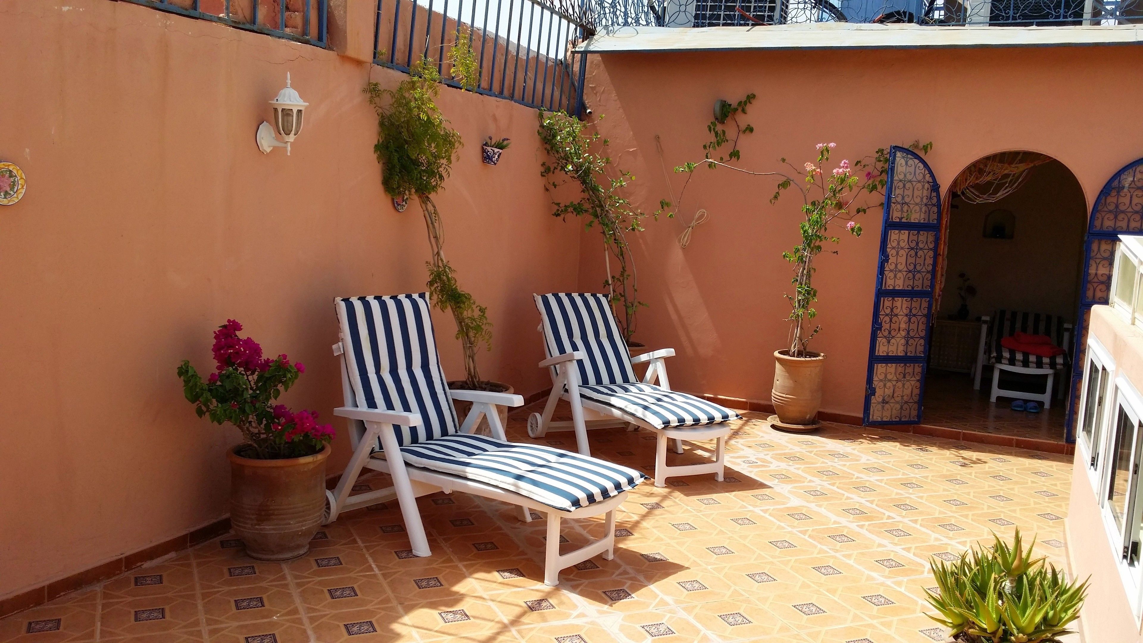 Un patio soleado con dos sillones a rayas, una planta en maceta y piso de baldosas.