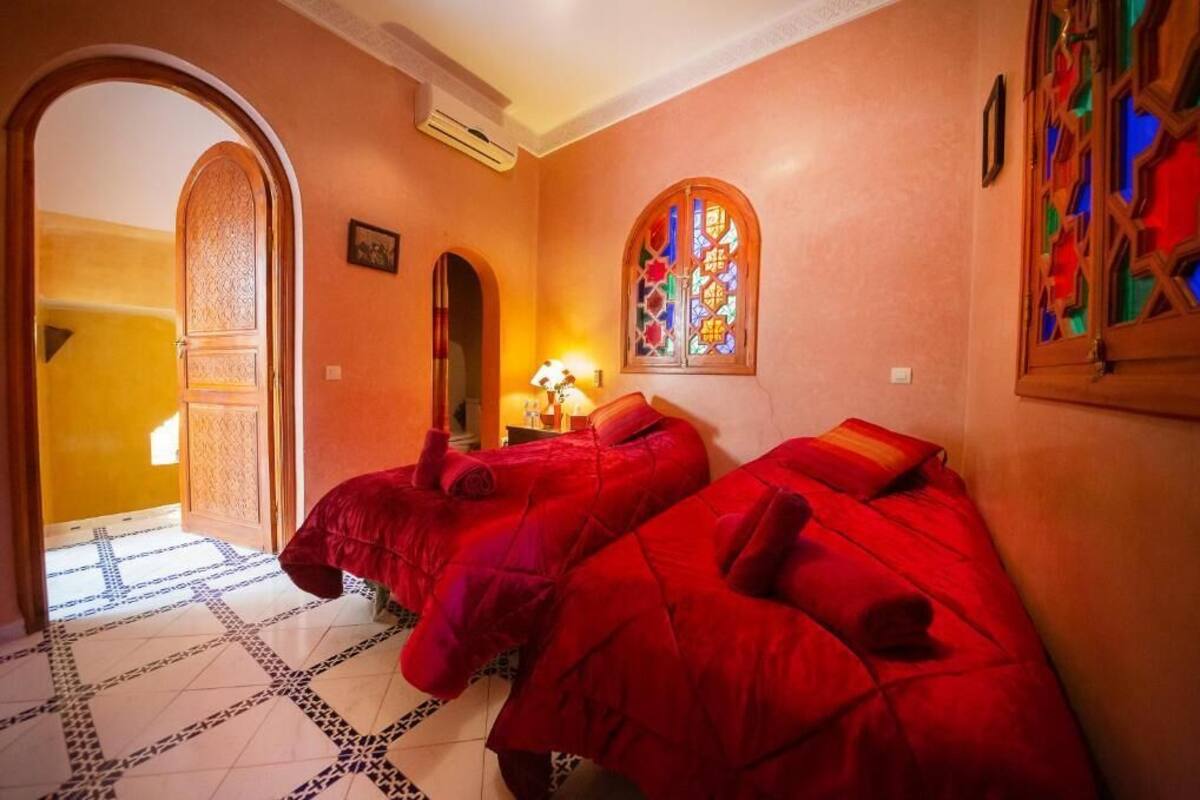 A room with two red beds, a stained glass window, and a tiled floor.