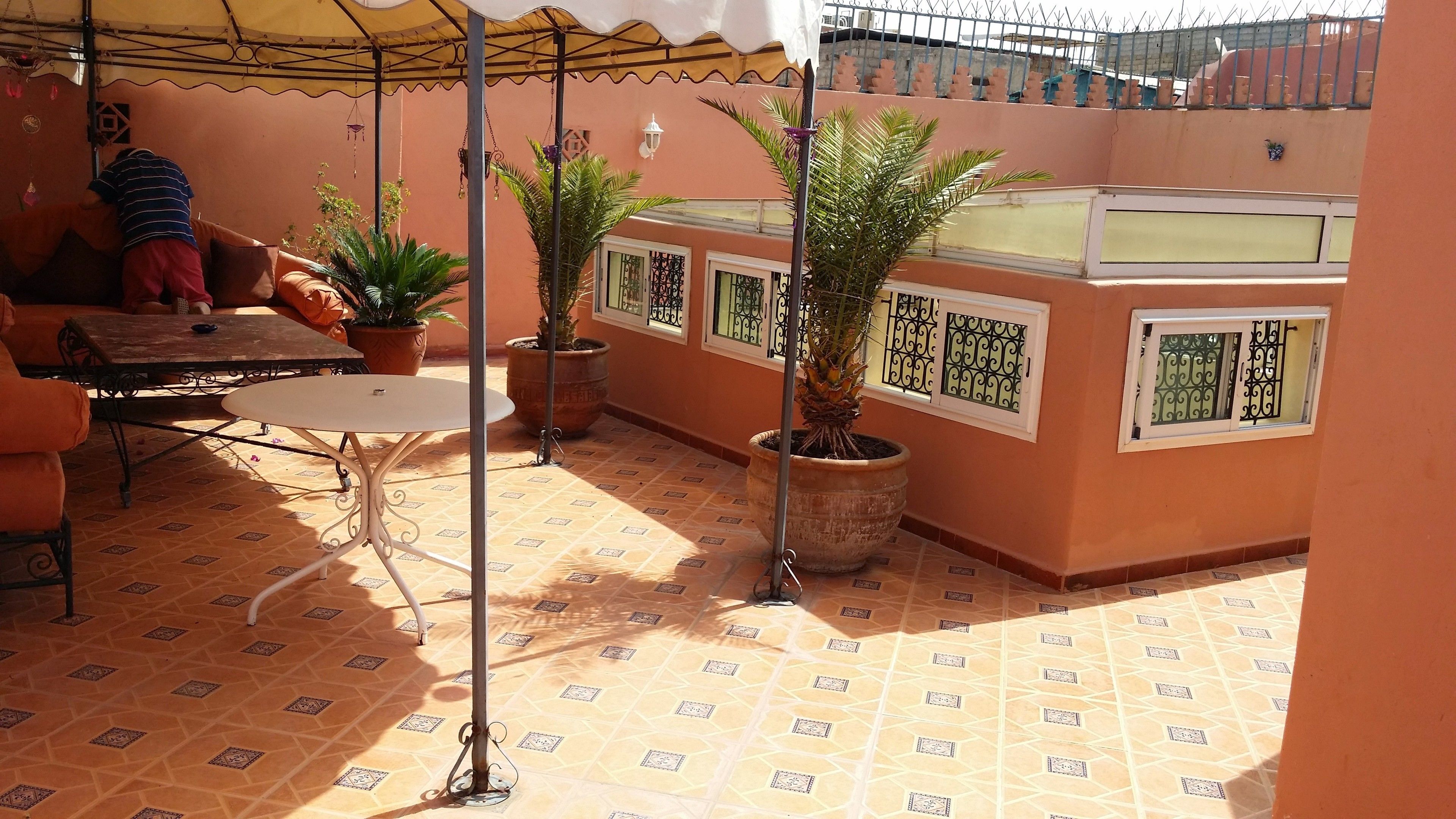 A covered patio area with a table and chairs, potted plants, and a tiled floor.