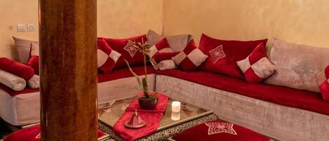 A cozy room with a sofa adorned with red and beige cushions, a small table with a candle, and a decorative plant.
