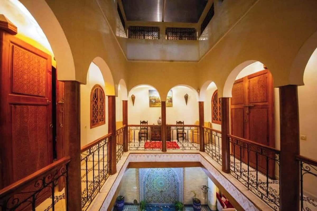 A corridor with arched ceilings, wooden doors, and a central pool area with a patterned floor.