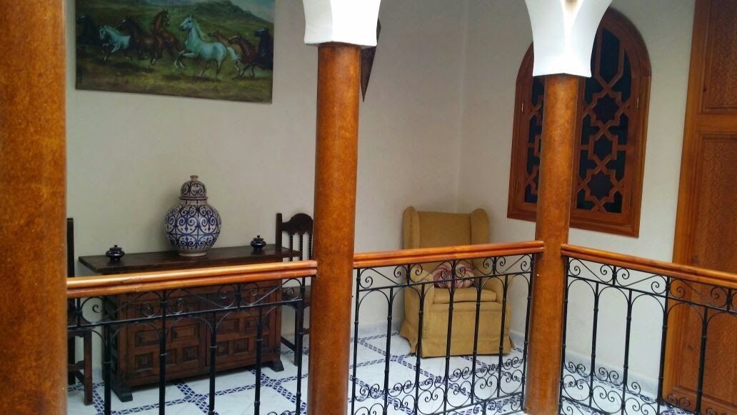 A staircase with a patterned floor, a wooden bench, a decorative vase, and a painting of horses.