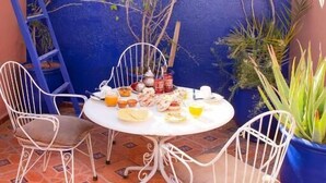A patio with a round table, white metal chairs, and a blue wall. - Riad La Lune de Marrakech  (Marrakech)