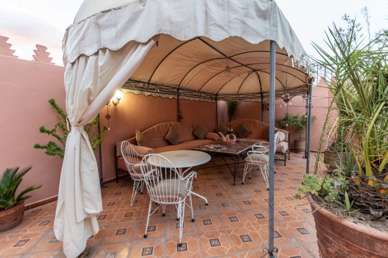 A covered outdoor seating area with a table and chairs, a sofa, and potted plants.