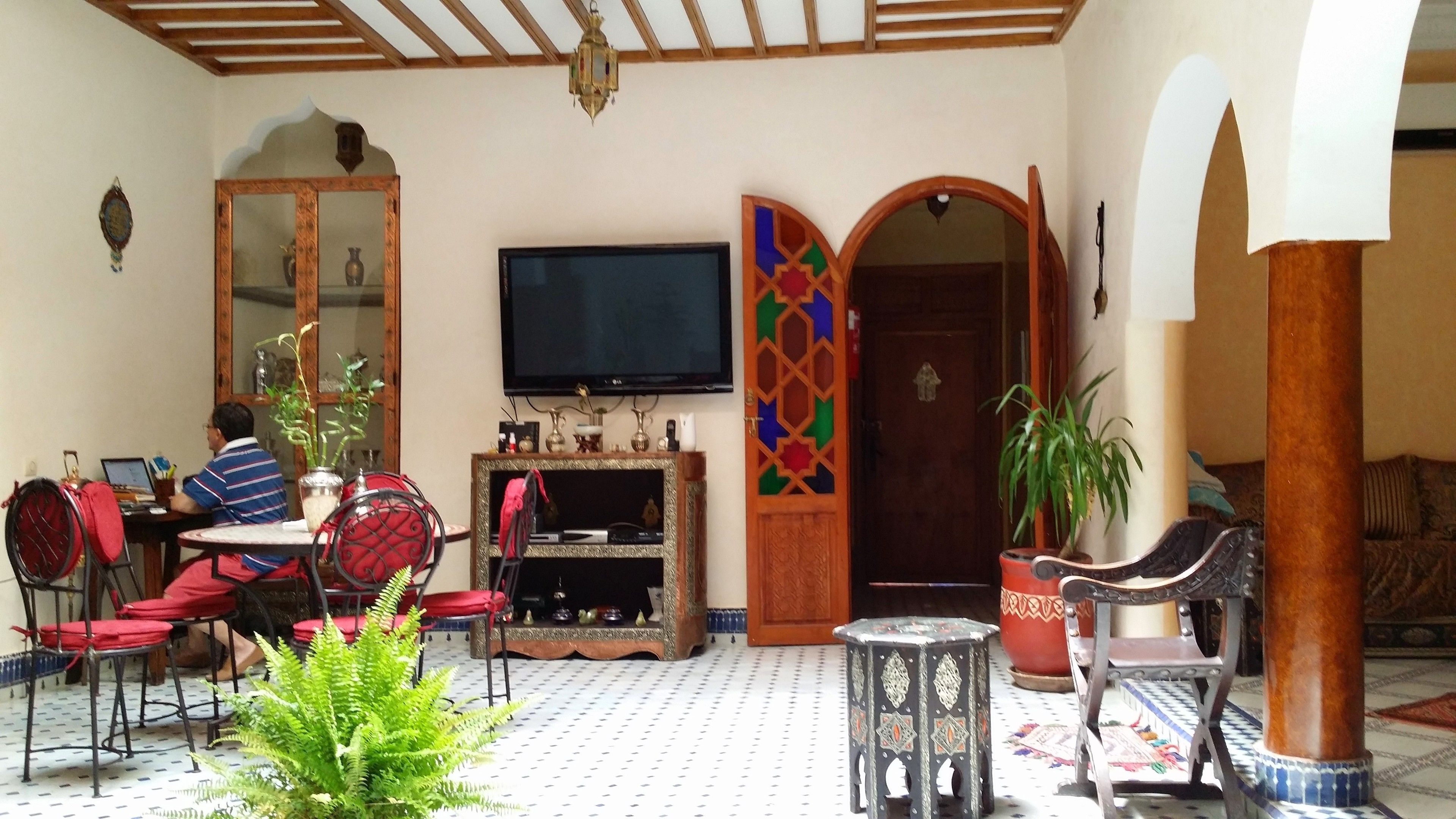 A living room with a television, a sofa, a dining table with chairs, and a decorative archway.