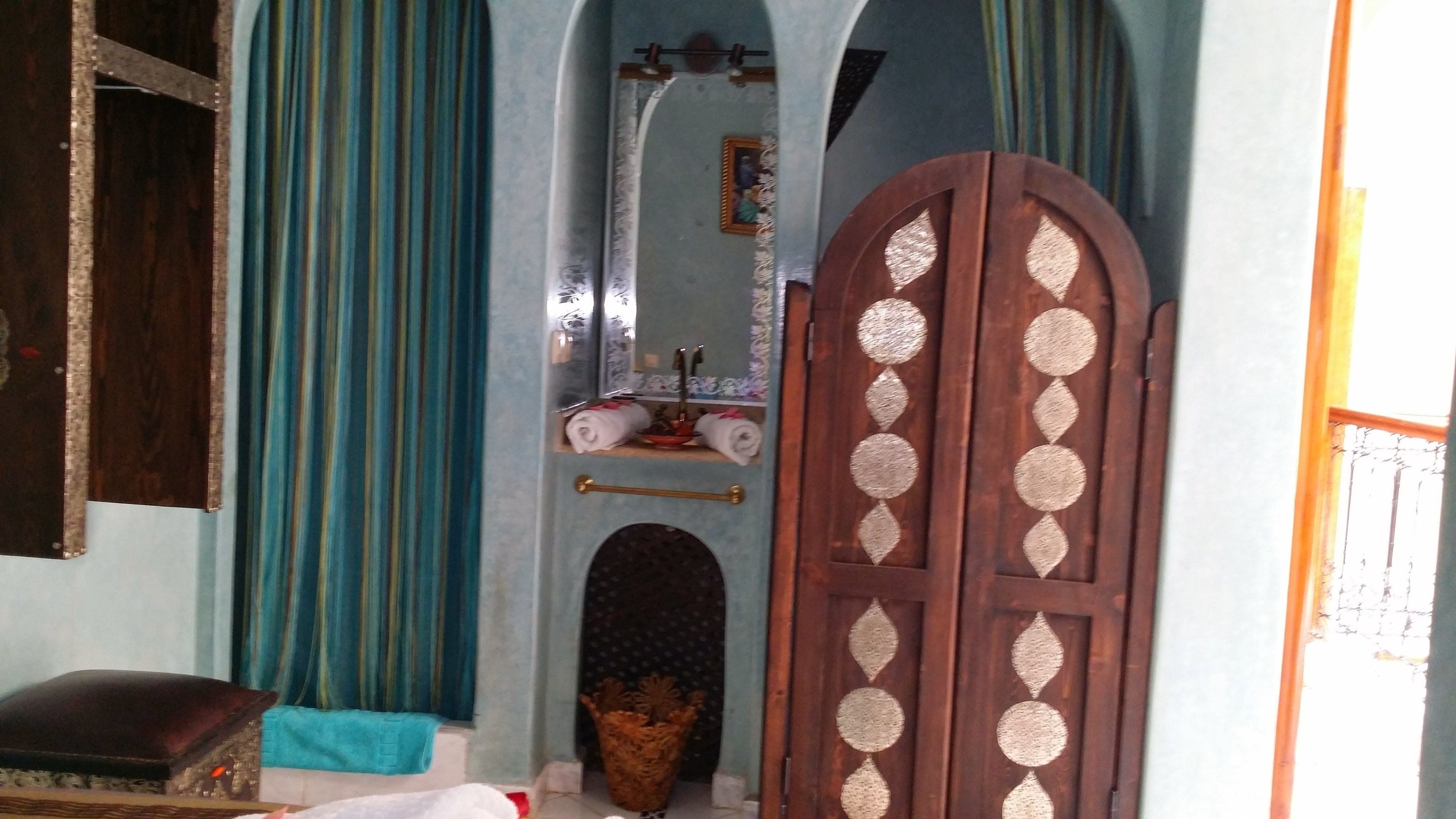 A room with a wooden door, a mirror, a small shelf with towels, and a patterned rug.