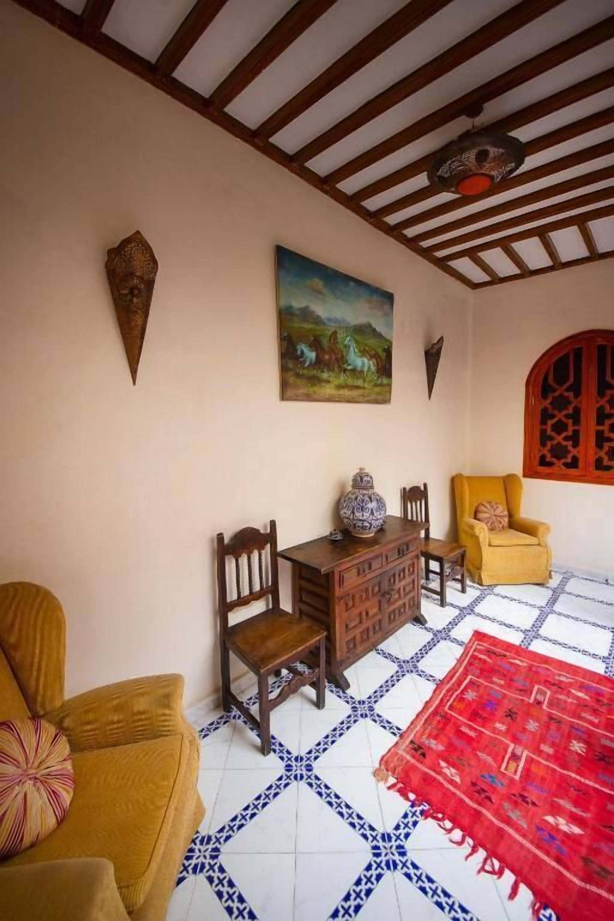 A room with a wooden ceiling, a painting, a red patterned rug, and a yellow armchair.