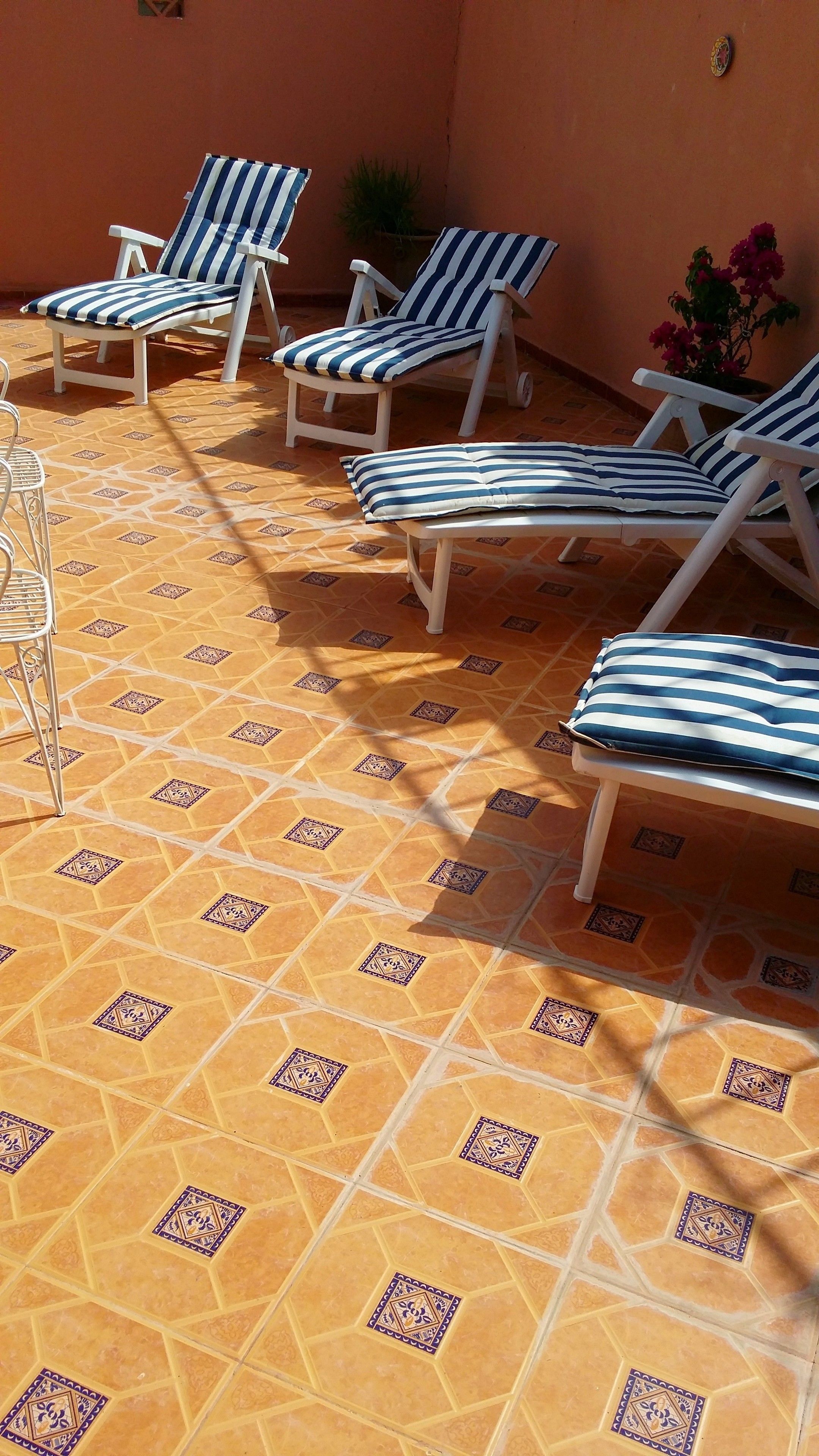 Area esterna con posti a sedere illuminata dal sole, caratterizzata da piastrelle a motivo esagonale e poltrone da lounge a righe.