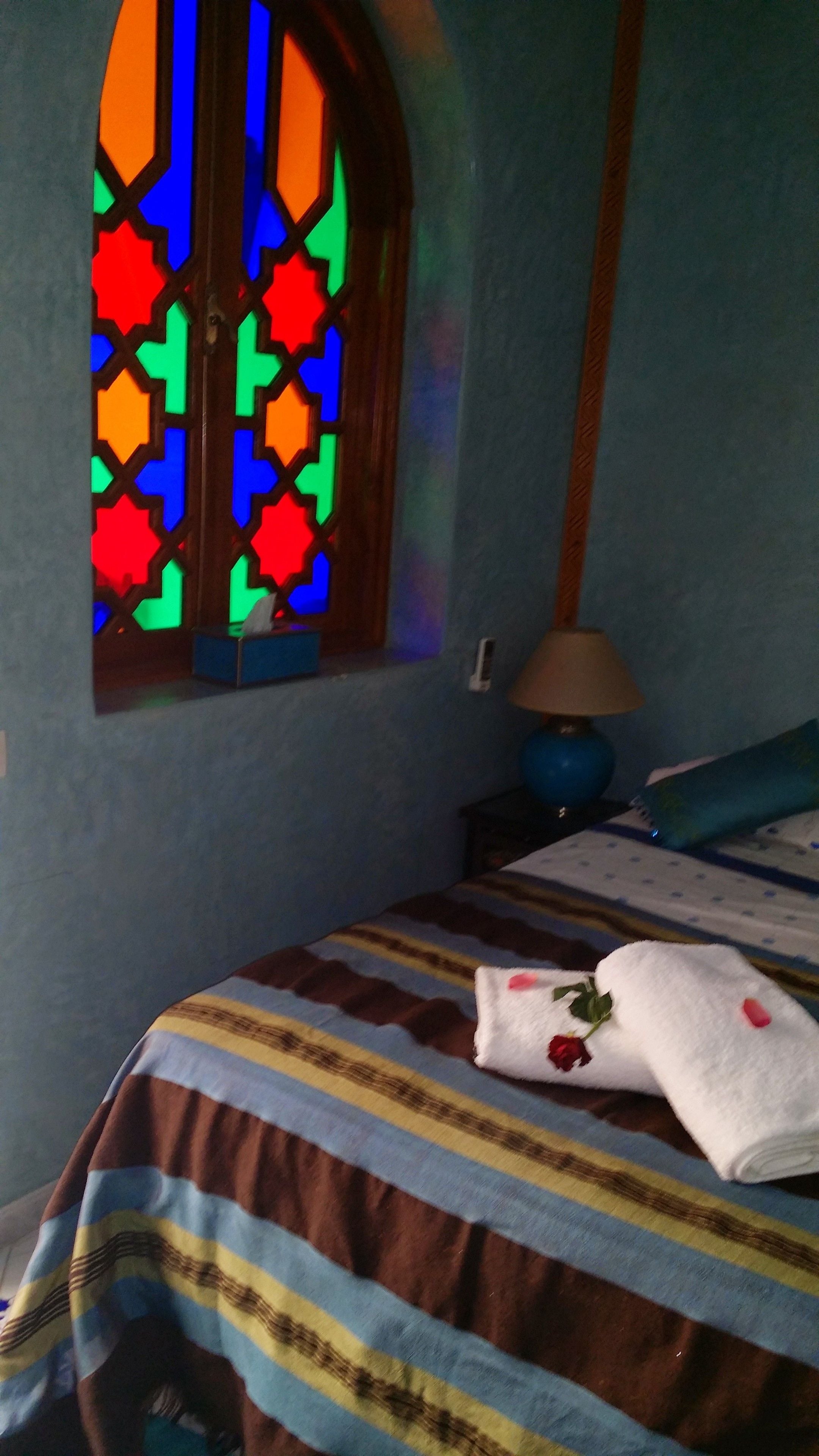 A bedroom with a bed, a window with stained glass, a lamp, and a striped bedspread.