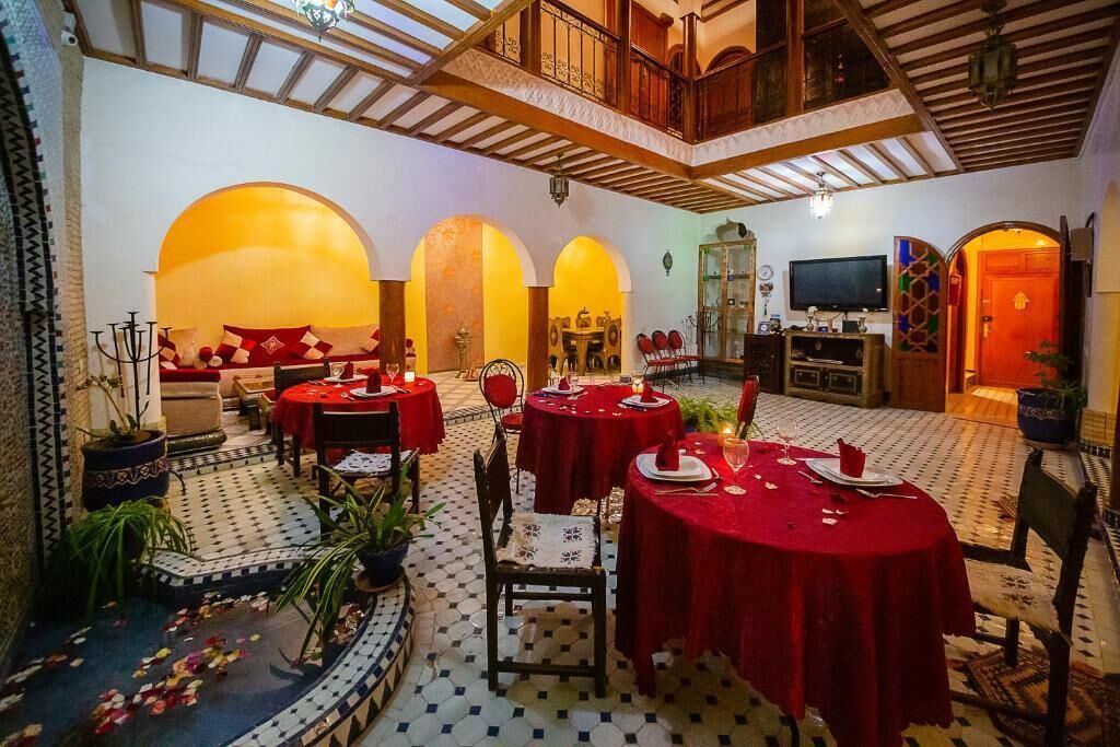 A dining area with multiple tables set for a meal, featuring a high ceiling with wooden beams and a television mounted on the wall.