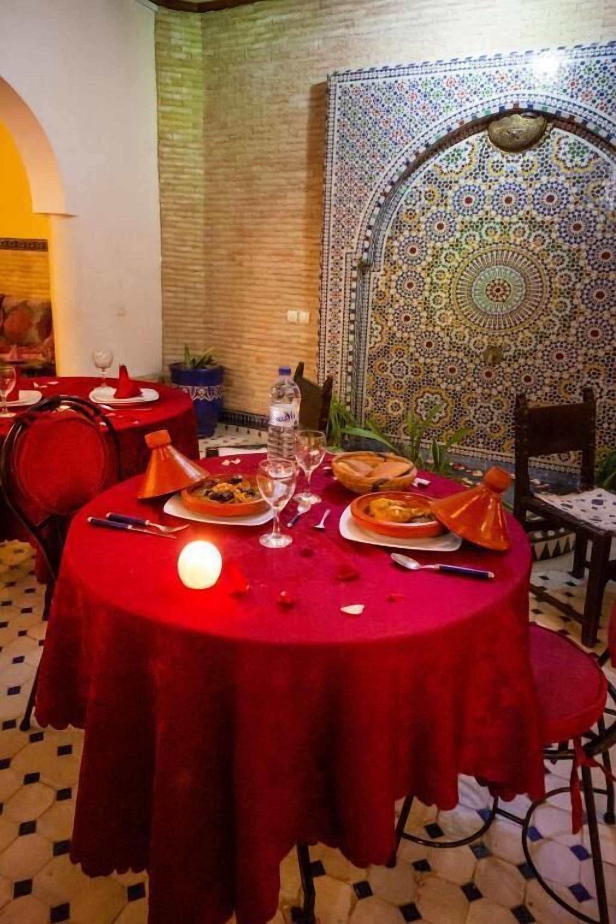 Un comedor con mantel rojo, pared de azulejos marroquíes y techo estampado.