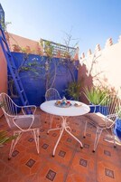 Un pequeño patio exterior con una mesa redonda y cuatro sillas blancas de metal.