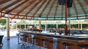 A covered outdoor bar area with a checkered floor, a pool in the background, and a person working at the bar. - Fantasy (Rhodes)
