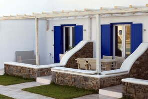 A covered outdoor seating area with stone walls and blue shutters, featuring a table and chairs.