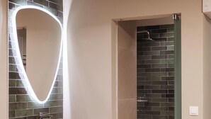 A bathroom with a black sink, a mirror with a light, and a shower area. - Fantasy (Rhodes)