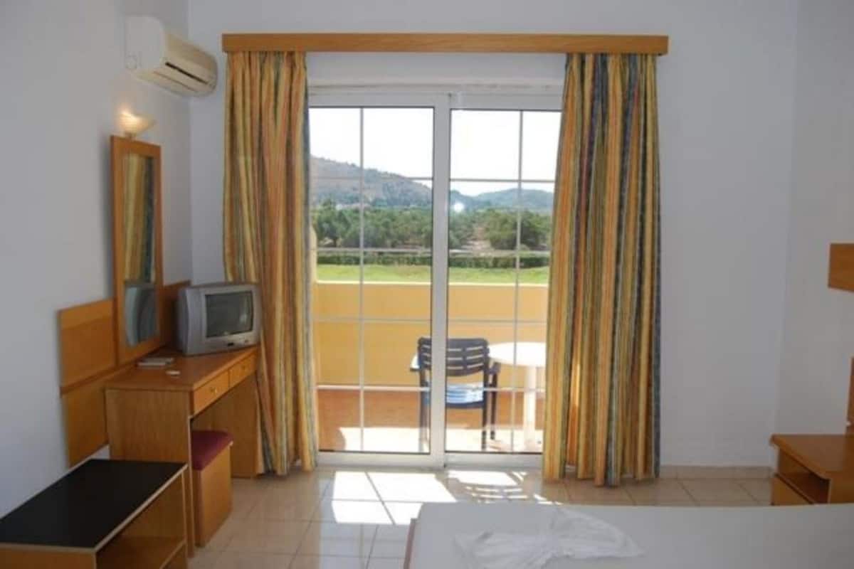 Habitación de hotel con cama, escritorio con televisor y puerta corrediza de vidrio que da a un balcón.