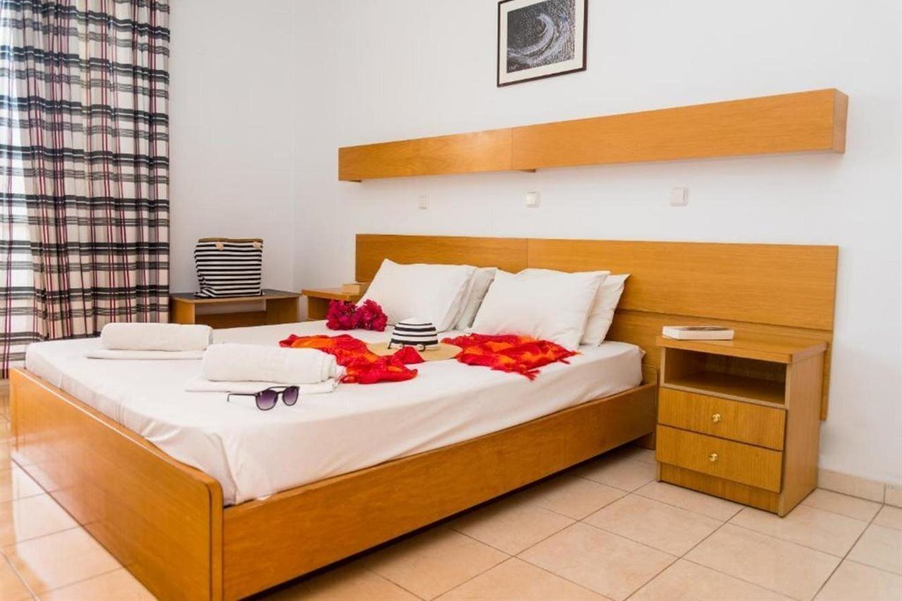 Una cama bien hecha con sábanas blancas, un cabecero de madera y una mesita de noche con una lámpara.