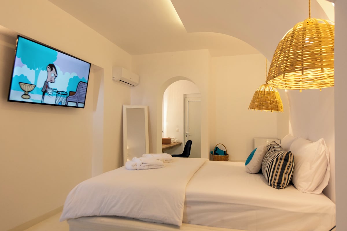 Un dormitorio con una cama, un televisor montado en la pared, un espejo y una lámpara de mimbre.