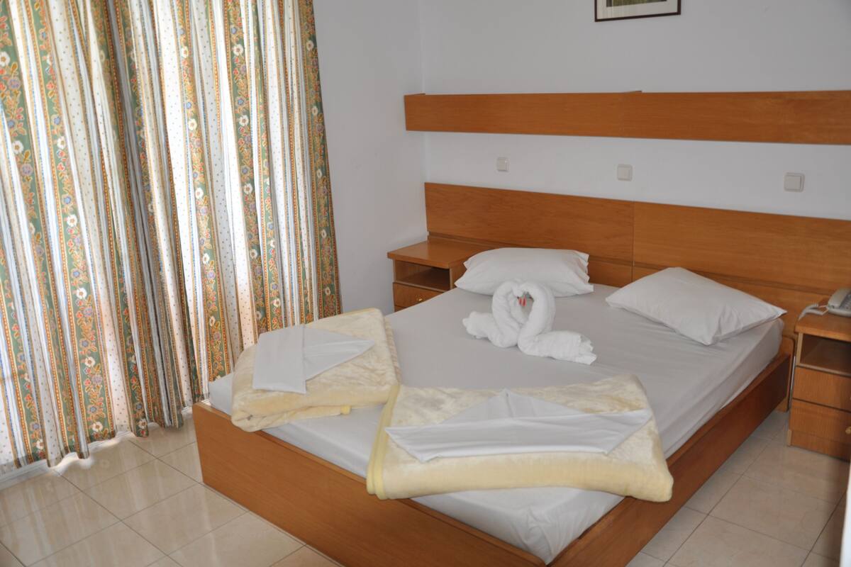 Una cama bien hecha con ropa de cama y toallas blancas, un cabecero de madera y una mesita de noche con un teléfono.