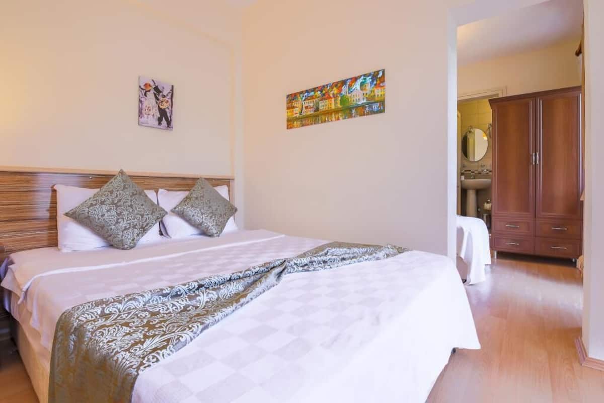 Habitación de hotel con una cama grande, dos almohadas, cabecero, un cuadro en la pared, un armario y un baño visible a través de una puerta abierta.
