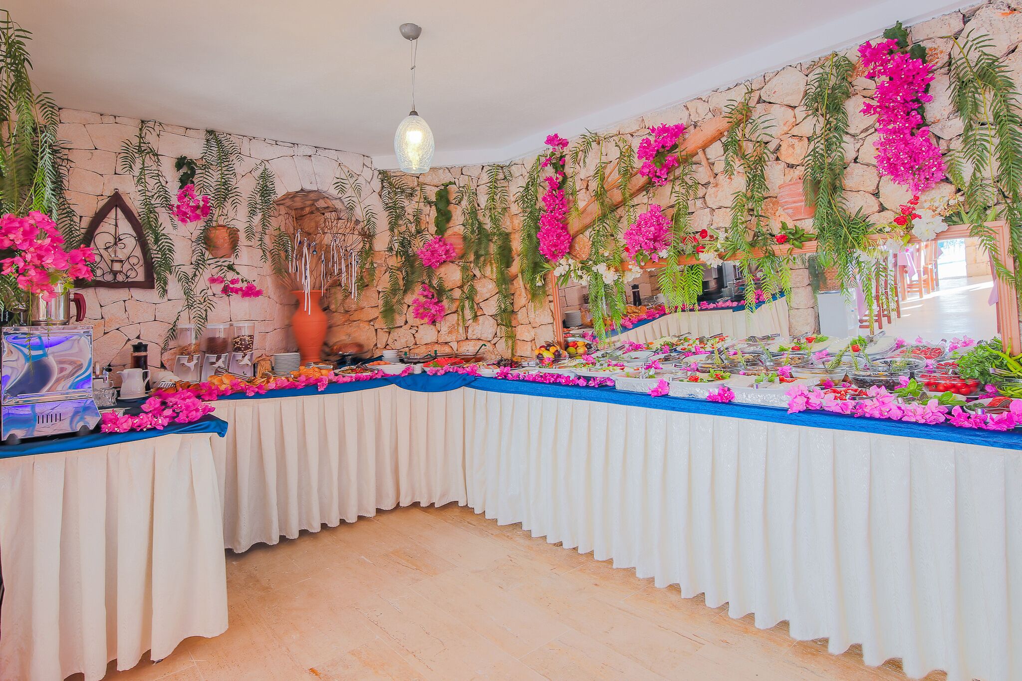 Una mesa de buffet con diversos alimentos, rodeada de plantas y flores colgantes.