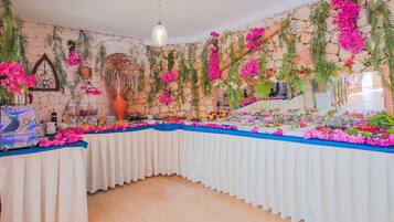 Una mesa de buffet con diversos alimentos, rodeada de plantas y flores colgantes.