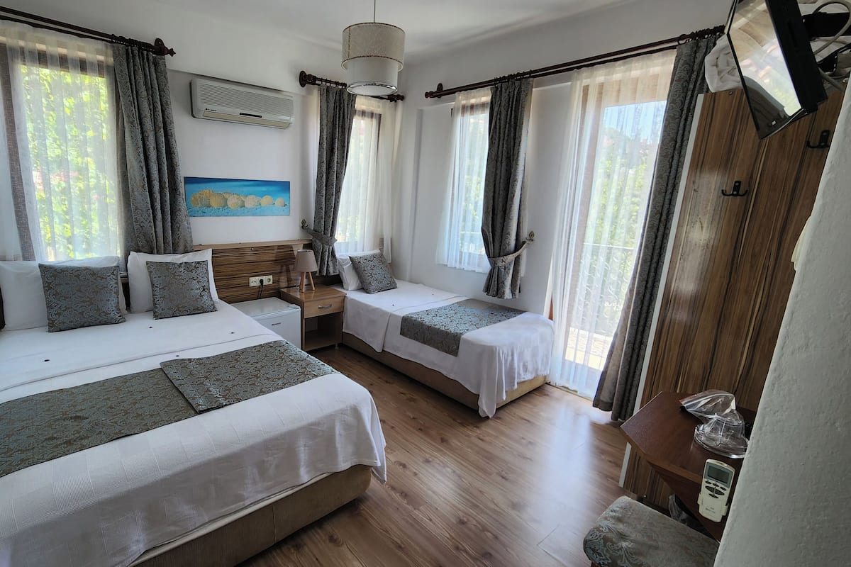 Una habitación de hotel con dos camas, piso de madera, una mesita de noche, una lámpara y un cuadro en la pared.