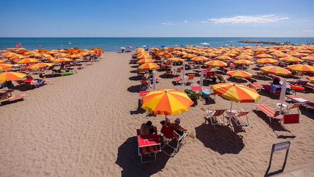 A beach with rows of sunbeds and umbrellas, a clear sky, and the ocean in the background.