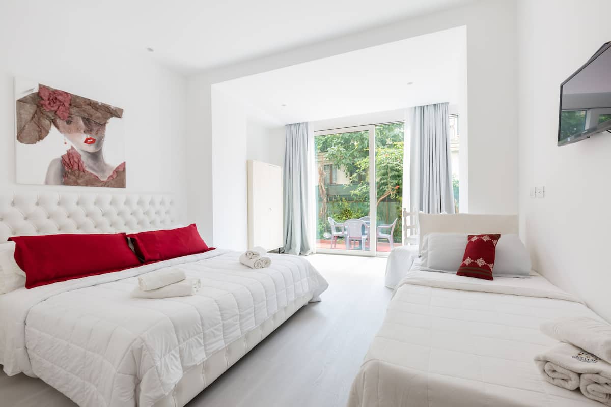 A hotel room with two beds, a large window, and a painting on the wall.
