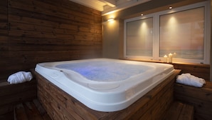 A hot tub in a wooden cabin with a window and candles.