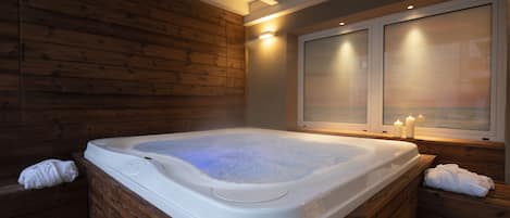 A hot tub in a wooden cabin with a window and candles.