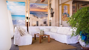 A modern living room with a white sofa, a wooden coffee table, and a large painting of a sunset over the ocean.