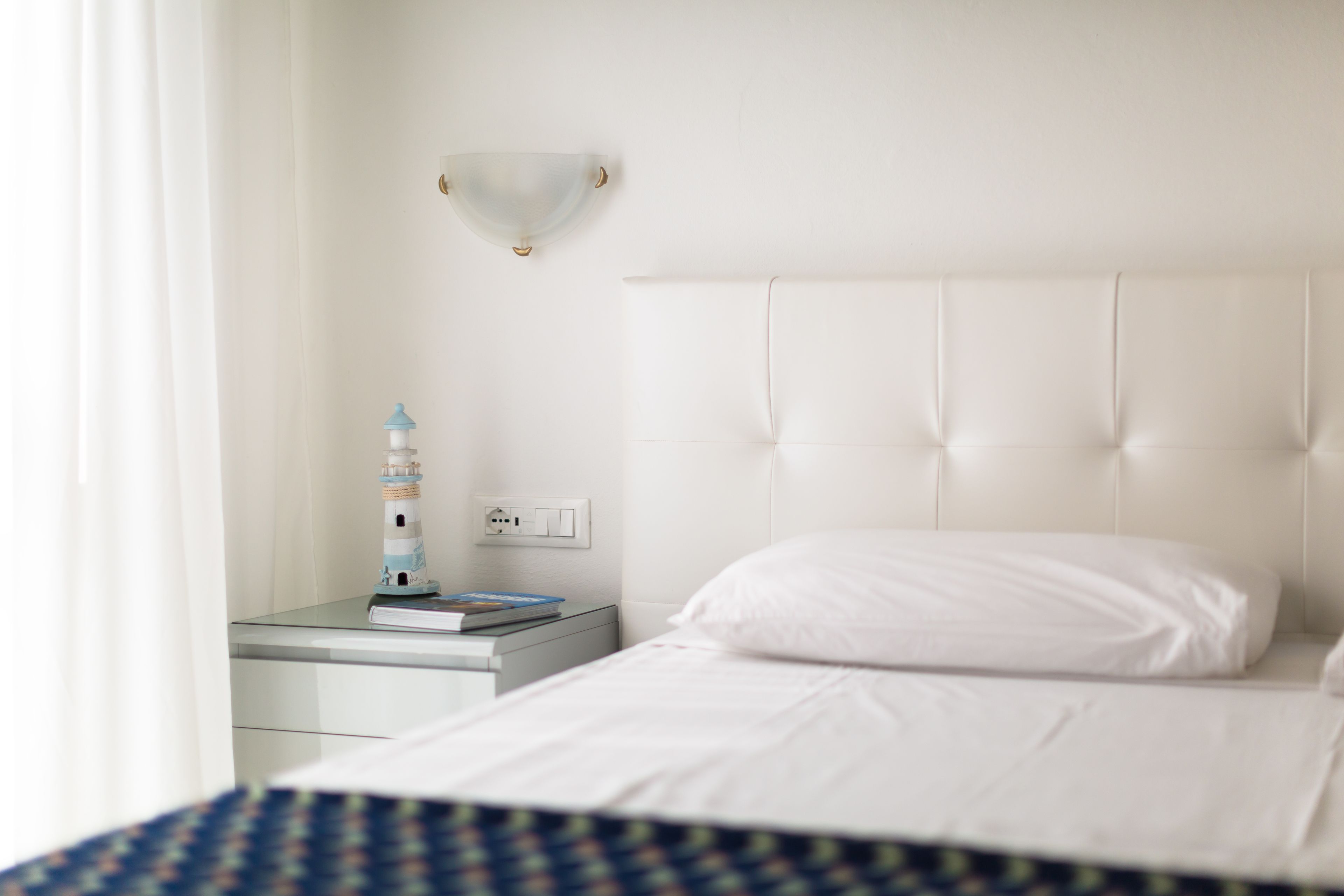 A hotel room with a neatly made bed, a bedside table with a lamp, and a wall-mounted light fixture.