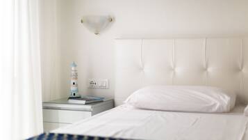 A hotel room with a neatly made bed, a bedside table with a lamp, and a wall-mounted light fixture.